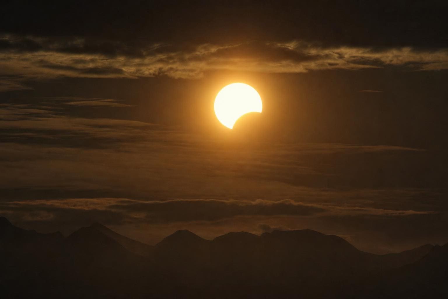 Teilweise verfinsterte Sonne als helle Sichel über einer Bergkette in Tirol