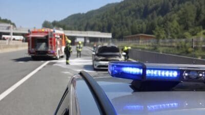 Blaues Blaulicht auf einem Polizeifahrzeug vor einem ausgebrannten PKW und Feuerwehrleuten auf der Autobahn