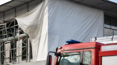 Rotes Feuerwehrfahrzeug vor einem Gebäude mit großer weißer Plane und Gerüst