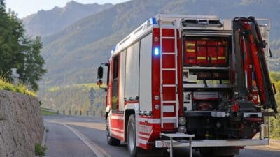Rotes Feuerwehrfahrzeug mit geöffnetem Geräteraum auf einer Straße vor Bergen