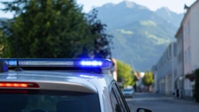 Nahaufnahme eines Polizeifahrzeugs mit leuchtendem Blaulicht und Bergkulisse im Hintergrund