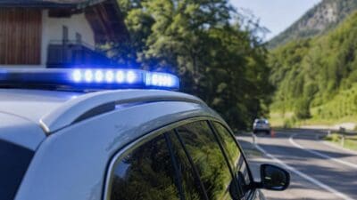 Blaues Blaulicht leuchtet auf dem Dach eines Polizeiwagens vor einer bergigen Landschaft mit Haus