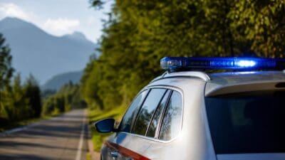 Heck eines silbernen Einsatzfahrzeugs mit blauem Blaulicht auf einer Landstraße vor Bergen