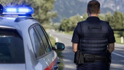 Polizist in Uniform steht neben Streifenwagen mit Blaulicht auf einer Bergstraße