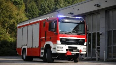 Rotes und weißes Feuerwehrfahrzeug mit Blaulicht vor einem Gebäude