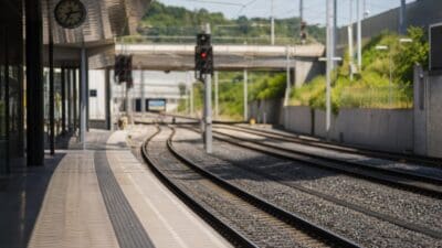 Leerer Bahnsteig mit Uhr neben Gleisen mit roten Signalen und grünen Hügeln