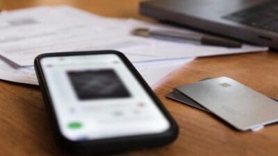 Smartphone mit geöffneter App liegt auf einem Holztisch neben Kreditkarten und Papieren.