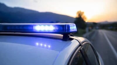 Blaues Blaulicht leuchtet auf dem Dach eines weißen Polizeifahrzeugs an einer Straße mit Bergpanorama.