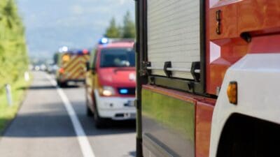 Rotes Feuerwehrfahrzeug und weiteres Einsatzfahrzeug mit Blaulicht auf der Autobahn vor Bergen