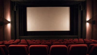 Leerer Kinosaal mit Reihen roter Polstersessel und heller Leinwand