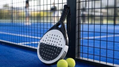 Padel-Schläger lehnt an einem Pfosten mit zwei gelben Bällen auf blauem Spielfeld