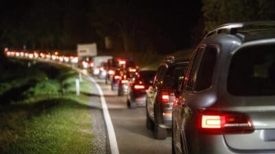 Mehrere Fahrzeuge mit leuchtenden Rücklichtern bilden einen Stau auf einer nächtlichen Landstraße.