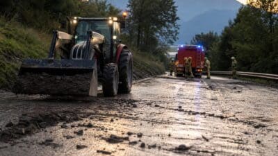 Ein Traktor mit Frontlader entfernt Schlamm und Steine von der nassen Fahrbahn.