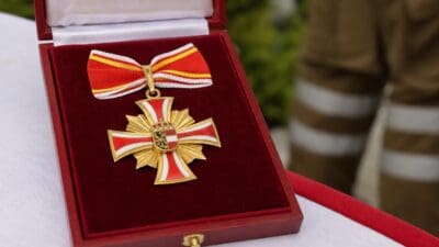 Goldenes Steckkreuz mit rot-weißer Schleife und Wappen in roter Samtschachtel