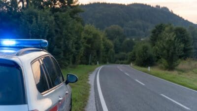 Polizeifahrzeug mit blauem Blaulicht parkt am Straßenrand einer kurvigen Landstraße