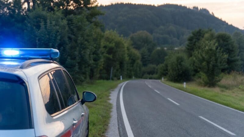 Polizeifahrzeug mit blauem Blaulicht parkt am Straßenrand einer kurvigen Landstraße