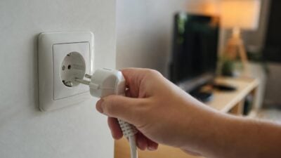 Eine Hand steckt einen weißen Stecker in eine weiße Steckdose an der Wand.