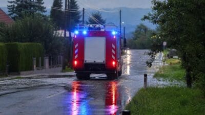 Heckansicht eines roten Feuerwehrfahrzeugs mit blauem Blaulicht auf nasser Straße bei Dämmerung