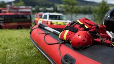 Rotes Schlauchboot mit rotem Helm und Rettungstaschen vor Einsatzfahrzeugen am Gewässer