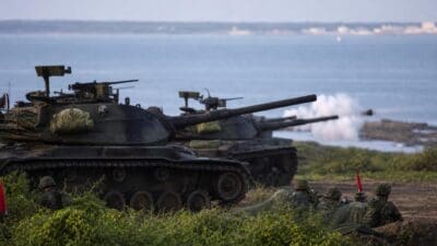 Mehrere Kampfpanzer feuern von einem Strand aus ins Meer.
