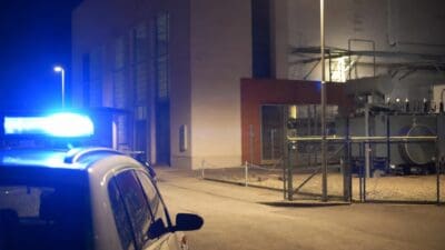 Weißes Polizeifahrzeug mit blauem Blaulicht vor Kraftwerksgebäude bei Nacht