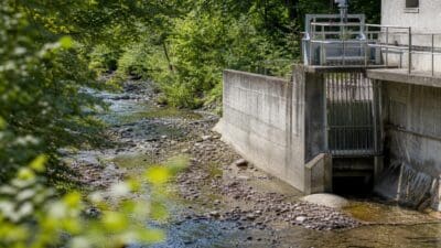 Niedriger Wasserstand in einem Fluss mit steinigem Bett und einem Betonbauwerk eines Wasserkraftwerks