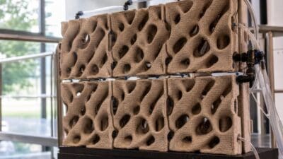 Beigefarbene poröse Keramikstruktur mit Wellenform und angeschlossenen transparenten Wasserleitungen.