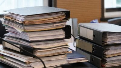 Mehrere Stapel von Aktenordnern und losen Dokumenten auf einem Schreibtisch