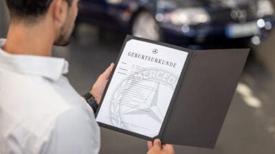 Ein Mann hält eine geöffnete Mappe mit der Mercedes-Benz Geburtsurkunde in der Hand.