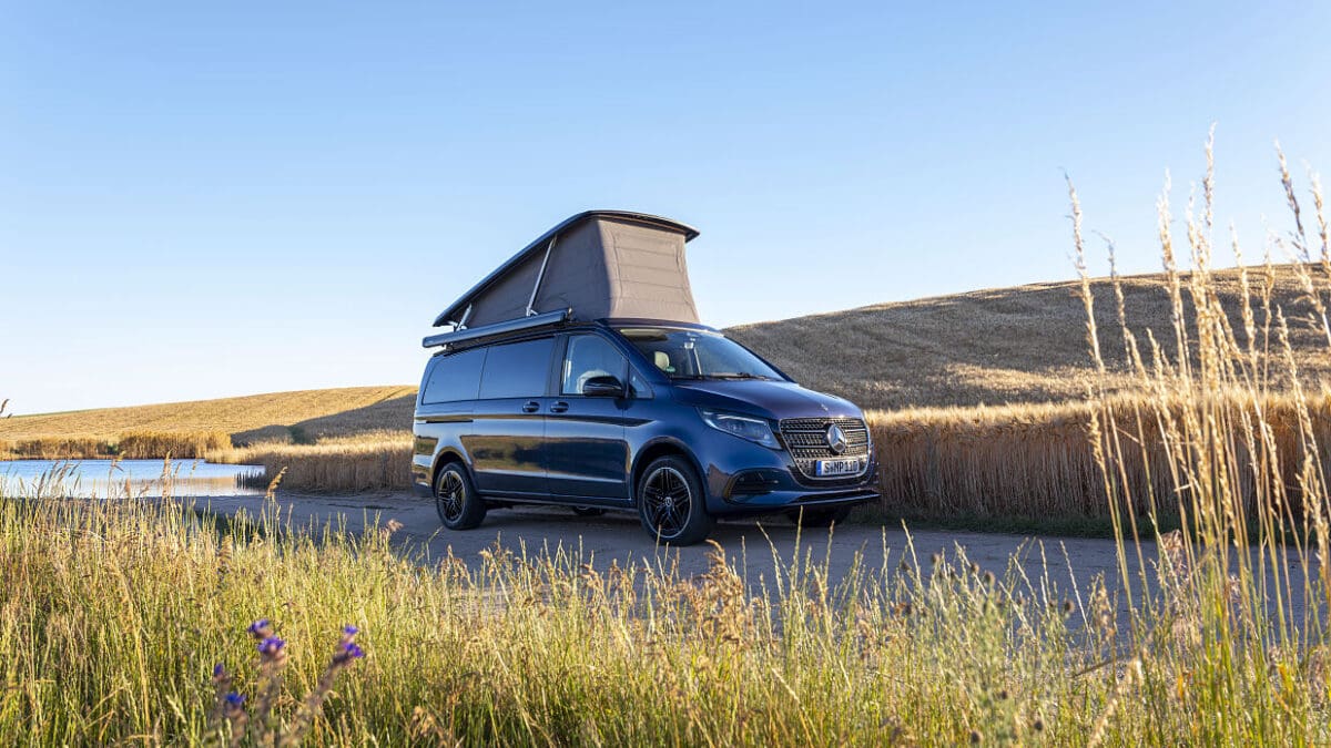 Dunkelblauer Mercedes-Benz Campervan mit aufgestelltem Dach auf einem Weg in der Natur