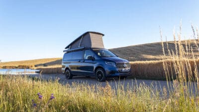 Dunkelblauer Mercedes-Benz Campervan mit aufgestelltem Dach auf einem Weg in der Natur