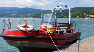 Rotes Rettungsboot der Wasserrettung mit Blaulicht und Rettungsring liegt am Holzsteg an einem See