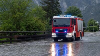 Rotes Feuerwehrauto mit Blaulicht fährt durch Wasser auf einer Straße