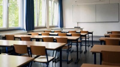 Leerer Klassenraum mit Reihen von Tischen und Stühlen sowie einer Tafel an der Wand