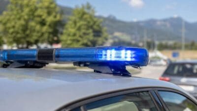 Leuchtendes blaues Polizeilicht auf dem Dach eines Einsatzfahrzeugs mit Bergpanorama im Hintergrund.