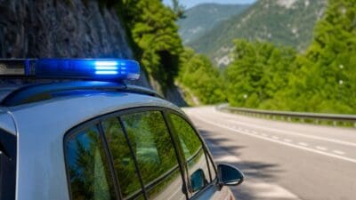 Heck eines silbernen Polizeiautos mit blauem Blaulicht auf einer kurvigen Straße in den Bergen
