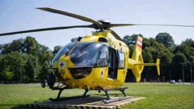 Gelber Rettungshubschrauber mit roten Kreuzen und geöffneter Tür auf einer Wiese