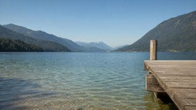 Ein hölzerner Steg am Ufer des klaren Weissensees mit Bergen im Hintergrund