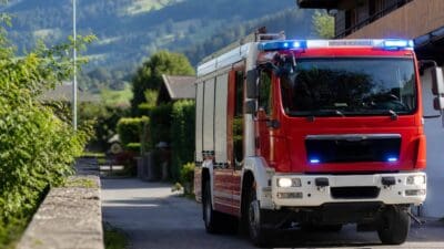 Rotes Feuerwehrfahrzeug mit aktiviertem Blaulicht auf einer Straße vor Berglandschaft
