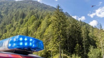 Blaues Blaulicht auf einem roten Einsatzfahrzeug mit Hubschrauber über bewaldeten Bergen