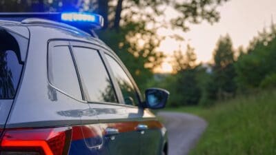 Heck eines Polizeifahrzeugs mit eingeschaltetem Blaulicht auf einer Straße bei Sonnenuntergang