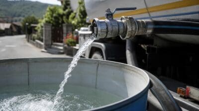 Wasser strömt aus einem Anschluss eines Tanklastwagens in einen großen blauen Behälter.