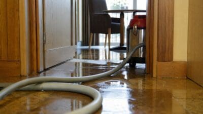 Wasser auf dem Boden eines Hotelzimmers mit Schlauch und rotem Sauggerät in der Türöffnung