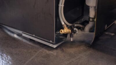 Wasser tropft aus der gebrochenen Zuleitung unter einem Kaffeeautomaten auf den dunklen Boden