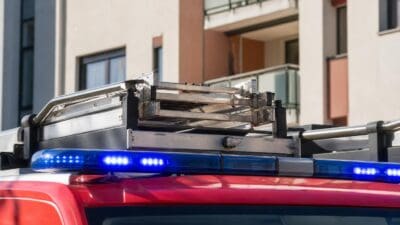 Blaues Blaulicht auf dem Dach eines roten Feuerwehrfahrzeugs vor einem mehrgeschossigen Wohnhaus