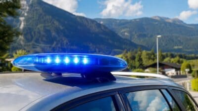 Blaues Blaulicht auf dem Dach eines Polizeifahrzeugs vor einer Berglandschaft.