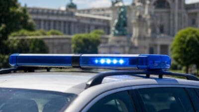 Ein leuchtender blauer Lichtbalken auf dem Dach eines Polizeifahrzeugs vor unscharfem Hintergrund.