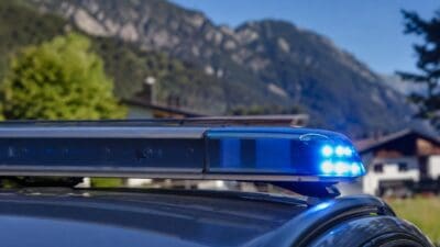 Blaues Blaulicht leuchtet auf dem Dach eines Polizeifahrzeugs vor einer Bergkulisse.