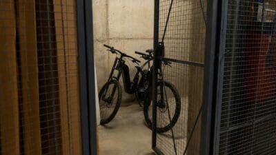 Zwei schwarze E-Bikes stehen in einem Kellerabteil hinter einem geöffneten Gittertor.