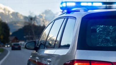 Heckansicht eines Polizeifahrzeugs mit leuchtendem blauem Blaulicht vor Bergpanorama